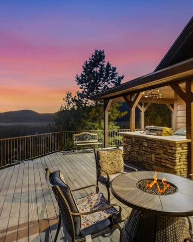 Expansive deck with fire pit, seating, and covered patio overlooking forested mountains at sunset